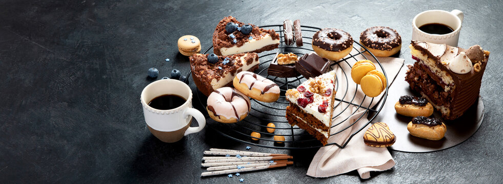 Table with various cookies, donuts, cakes, cheesecakes on dark background.