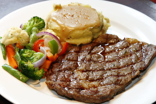 closeup of sirloin steak dish with assorted vegetables and gravied mashed potatoes