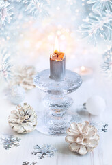 Christmas winter still life with burning candle, pine cones and snowflakes on light background.