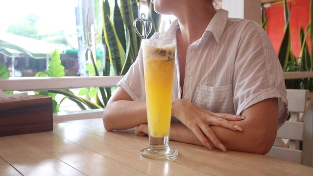A girl drinks a cocktail of fruits in a cafe, a shake of passion fruit