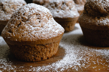 Close-up of a baked chocolate cupcake on a wooden board and sprinkled with white powdered sugar surrounded by other cupcakes