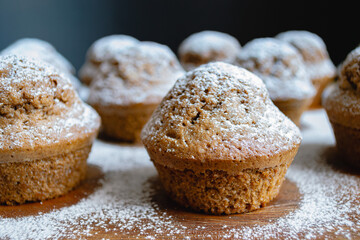 Close-up of a baked chocolate cupcake on a wooden board and sprinkled with white powdered sugar surrounded by other cupcakes