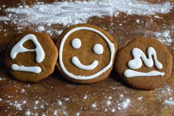 Three sweet cookies covered with white icing in the form of a smiley and the letters A and M lie on...
