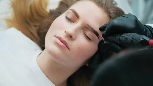 Blond model lying with eyes closed during permanent eyebrows makeup process