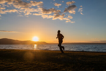 Fototapeta premium Silhouette image of a man running by Lake Rotorua at sunset, Rotorua, New Zealand.