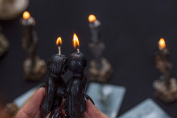 Black voodoo dolls in the form of lit candles in the hands of a witch. Love spells, rituals and...