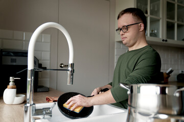 Adult caucasian man with down syndrome washing dishes at home