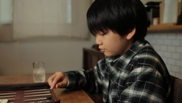 Japanese young boy playing backgammon at home. Roll dices. Profile.