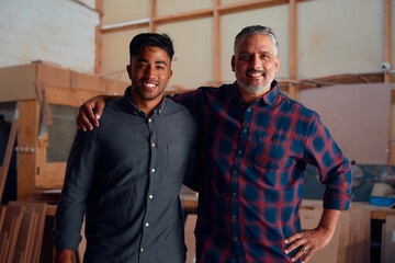 Group portrait of male colleagues smiling with arm around shoulder at woodworking factory