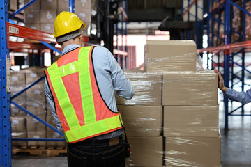 Rear veiw warehouse worker man with hardhat and reflective jackets wrapping boxes in stretch film parcel on pallet while control stock and inventory in retail warehouse logistics distribution center - obrazy, fototapety, plakaty