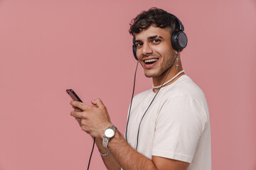 Brunette young man in headphones smiling while using mobile phone