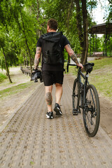 View from back on man walking with bicycle in park