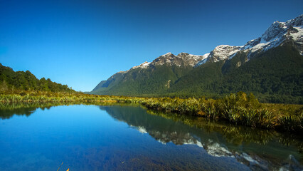 Mirror Lake at Fiordland National Park, Snowy mountains are reflecting in a calm water. New Zealand.