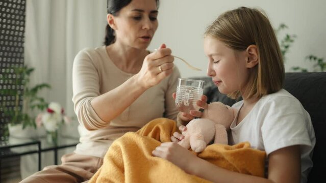 Mother gives ill sick child daughter medicine syrup at home. Mom woman cares about kid with fever and virus