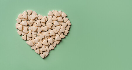 Heart shaped pet nutritional supplements over green background. Vitamin vegan treats for cats and dogs macro. Veterinary natural pills concept. Medicine for domestic animals. Copy space.