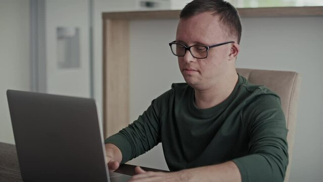 Focus adult caucasian man with down syndrome typing on laptop at home. Shot with RED helium camera in 8K.  