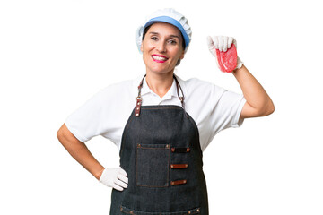 Butcher woman wearing an apron and serving fresh cut meat over isolated background posing with arms at hip and smiling