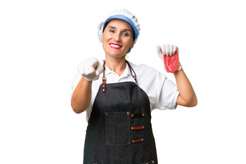 Butcher woman wearing an apron and serving fresh cut meat over isolated background pointing front with happy expression