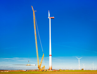 Construction work. Large wind power station nacelle on tower high up. Rotor with one blade....