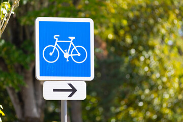 Señal de carril bici con una flecha a la derecha y el fondo de hojas de árbol desenfocadas (bokeh)