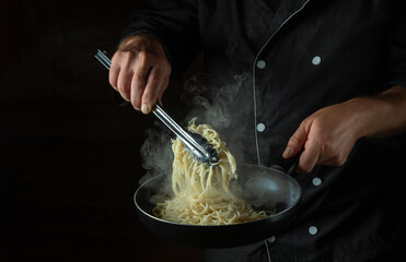 The cook fries spaghetti in a hot pan. Space for advertising on a black background. Italian national cuisine