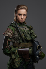 Shot of military woman with brown hairs and gas mask dressed in camouflage costume.