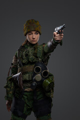 Studio shot of military woman dressed in camouflage uniform and hat aiming pistol.