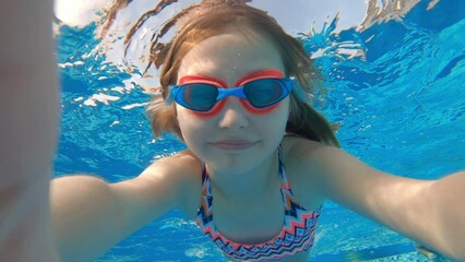 Cute little girl with goggles diving and swimming underwater in a pool. Kid taking selfie in water.