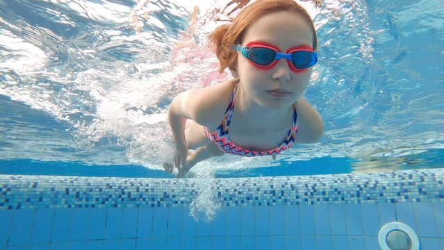 Cute little girl with goggles diving and swimming underwater in a pool