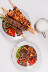 Delicious traditional Adana Kebab made with minced lamb and spices, chicken shish kebab, served with lavash, ayran Turkish buttermilk and roasted pepper tomato and red onion top view flat lay photo 