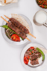 Delicious traditional chicken shish kebab and Adana Kebab made with minced lamb and spices, served with lavash, ayran Turkish buttermilk and roasted pepper tomato and red onion top view flat lay photo