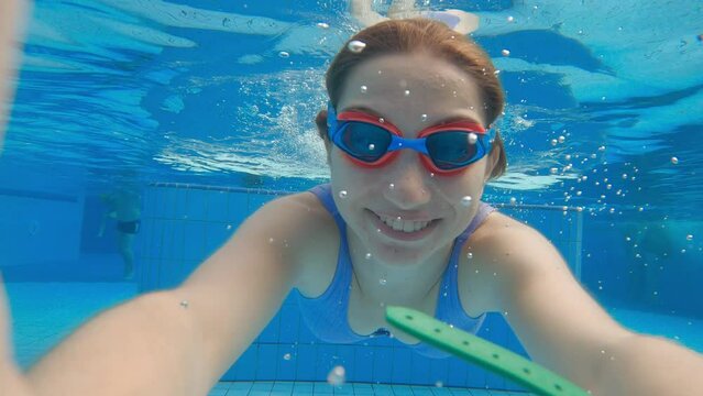 Cute little girl with goggles diving and swimming underwater in a pool. Child taking selfie in water.