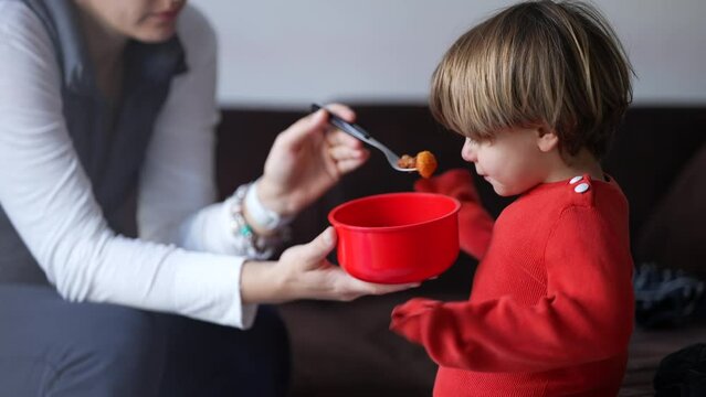 Candid mother feeding little boy son food. Parent giving gnocchi lunch meal