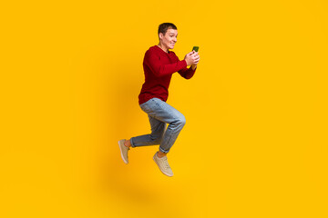 Fototapeta na wymiar Full body photo of handsome guy jumping high holding telephone rushing typing sms isolated yellow color background