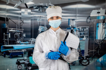 Naklejka premium doctor with stethoscope in operating room holding clipboard with operating room in background.