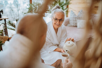 Senior couple in bathrobes enjoying time together in their living room, drinking hot tea, calm and...