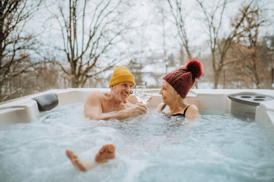 Senior couple in kintted cap enjoying together outdoor bathtub at their terrace during cold winter day.