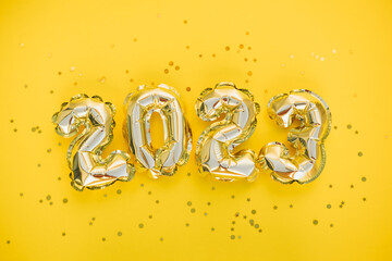 Happy New year and christmas holiday concept 2023. Gold balloons with glitter stars on yellow background. Gift card with space for text. Top horizontal view