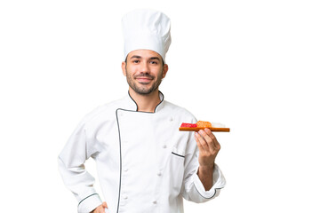 Young caucasian chef holding a sushi over isolated background posing with arms at hip and smiling