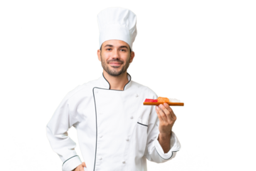 Young caucasian chef holding a sushi over isolated background posing with arms at hip and smiling