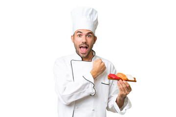 Young caucasian chef holding a sushi over isolated background celebrating a victory