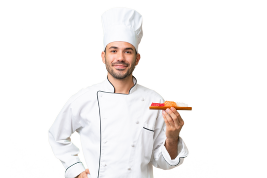 Young caucasian chef holding a sushi over isolated background posing with arms at hip and smiling