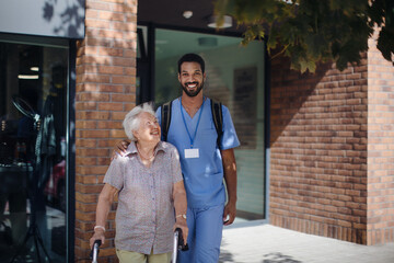 Caregiver walking with senior woman client in front of nurishing home.