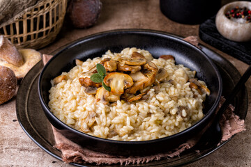 Risotto with porcini and champignon mushrooms in a black plate on brown background.