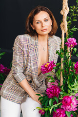 an attractive brunette woman in a plaid jacket on a swing with peony flowers.