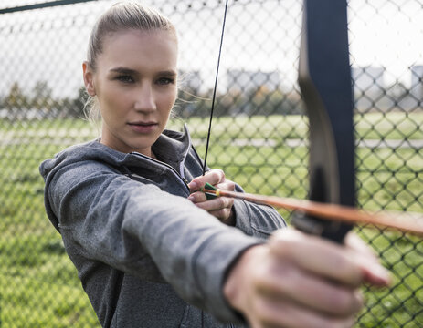 Confident sportswoman doing archery by fence