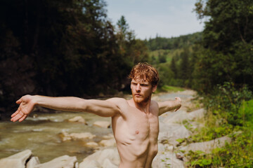 Fototapeta premium White young man wearing swimming trunks doing workout while resting by river