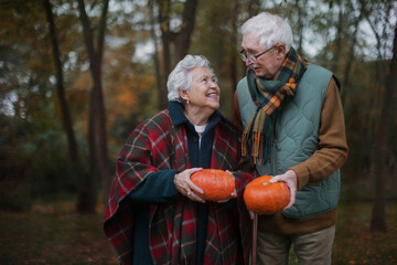 Senior couple with pumpkins in autumn forest.