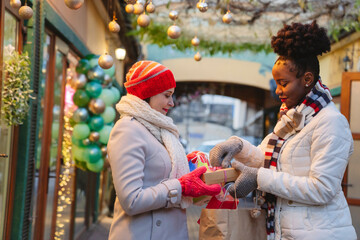 Woman in warm clothing giving gift to friend on Christmas festival