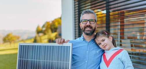 Father with his little daughter near their house with solar panels. Alternative energy, saving...